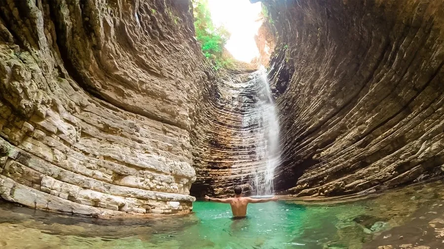Standing inside the narrow limestone gorge at Peshtura Waterfall, looking up at the falls dropping through the rock walls