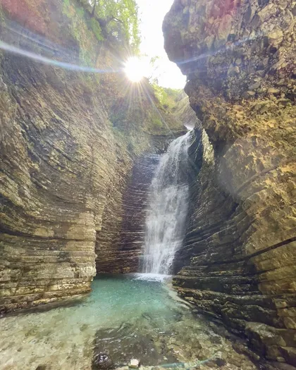 Sunlight breaking through the narrow gorge crack above Peshtura Waterfall as it drops into its pool